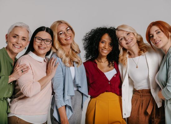 Multi-ethnic group of beautiful mature women bonding and smiling against grey background